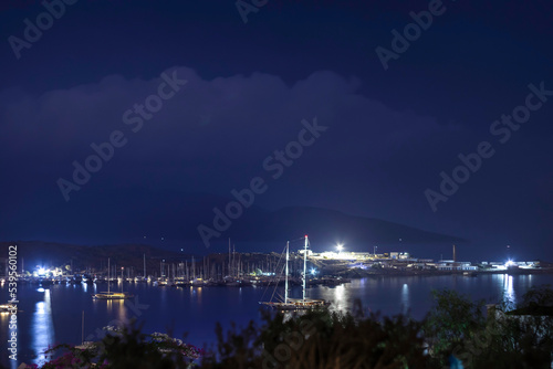 Boat on the sea, harbor and lights reflecting on the sea at blue hour on a rainy and cloudy evening.