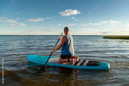 A man on his knees on a sup board in the evening at sunset.