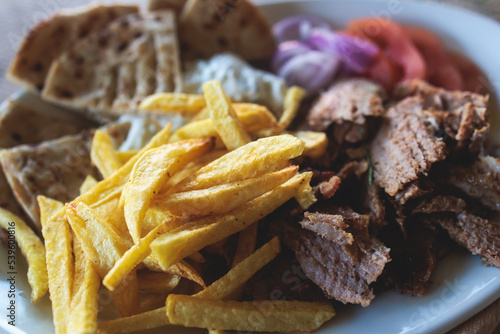 View of Gyros on a plate - traditional greek cuisine dish with kebab meat and pita bread with french fries and tzatziki sauce served in a cafe streets of Athens, Attica, Greece
