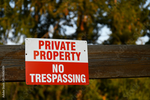 An image of a red and white no trespassing sign nailed to a wooden fence. 