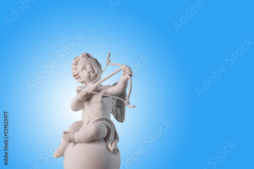 Figurine of an angel Cupid on the podium with a bow and arrow on a blu background . Valentine's Day.Place for text.