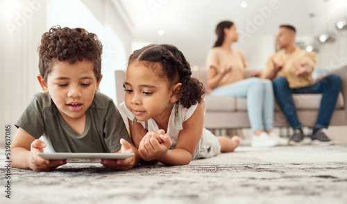 Kids on floor with tablet in living room, watching fun and educational videos or playing game online with parents on sofa. Technology, internet and children play on carpet with mobile app together.