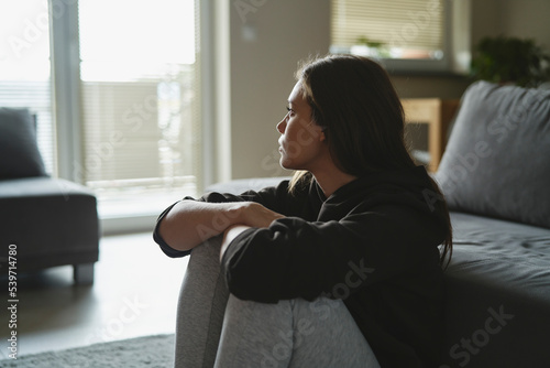 Caucasian sad woman sitting at the floor and looking throw window at home