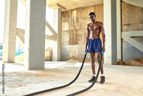 Rope workout. Sport man doing battle ropes exercise outdoor. Black male athlete exercising, doing functional fitness training with heavy rope