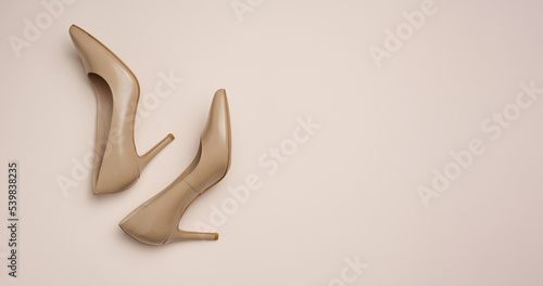 Leather beige high heel shoes on a beige background, top view