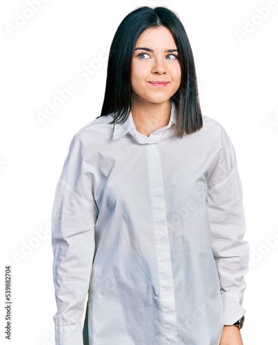 Young brunette woman with blue eyes wearing oversize white shirt smiling looking to the side and staring away thinking.