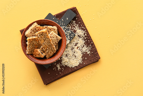 Board with bowl of tasty kozinaki and sesame seeds on color background