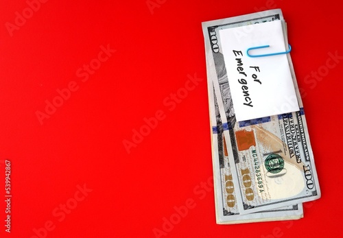 White paper note with text written FOR EMERGENCY clip with cash dollars money on red copy space background , smart financial planning to save money for contingency fund - for rainy day, future crisis