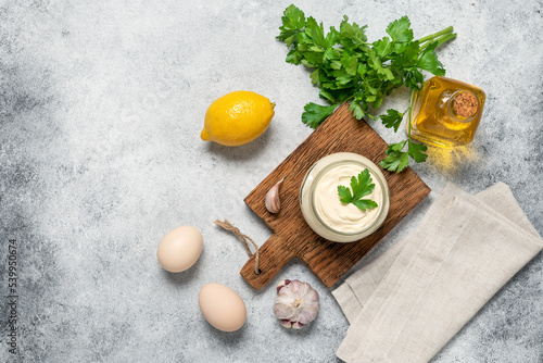 Aioli sauce with ingredients on a light grunge background. Homemade mayonnaise. Top view, flat lay, selective focus, copy space.