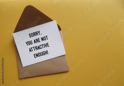 On copy space yellow background, envelope with note written SORRY, YOU ARE NOT ATTRACTIVE ENOUGH - concept of LOOKISM - discrimination treatment of people who are considered physically unattractive