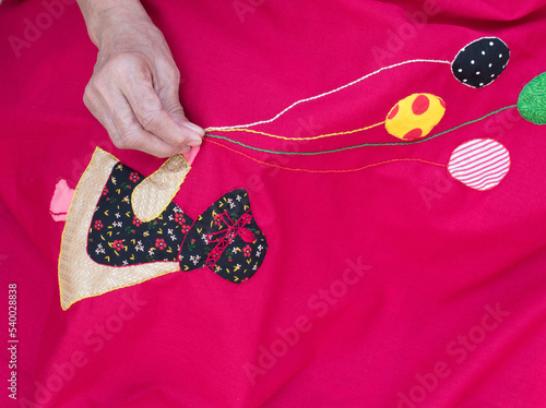Closeup of a woman's hands sewing applique work making doll and balloon with chain stich in baby’s quilt or bed sheet. Concept of self employment woman and Female entrepreneurs in India.