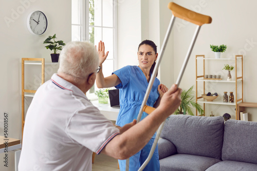 It's getting dangerous in here. Angry, aggressive, bad tempered senior patient fighting with medical worker. Old man becomes uncontrollable and threatens scared nurse or volunteer medic with crutch