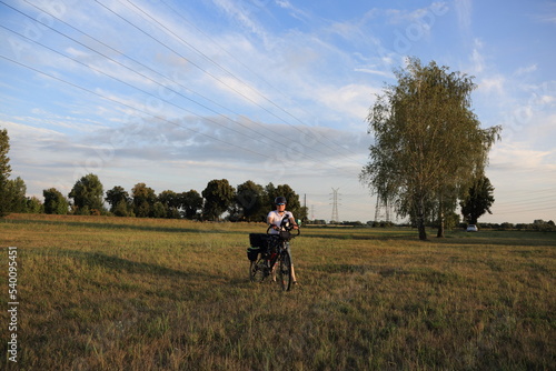 Mężczyzna z rowerem turystyczny na łące, w tle brzozy. 