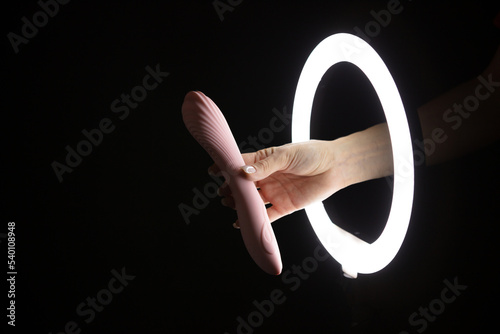 Female hand holding vibrator through led ring lamp on black background. Sex concept