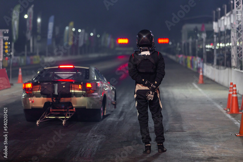 Dragster driver with drag car in race track at night, Drag racing car at the start competition at night, Drag race car in race track at night, Sport car at the start, speed competition, drag racing.