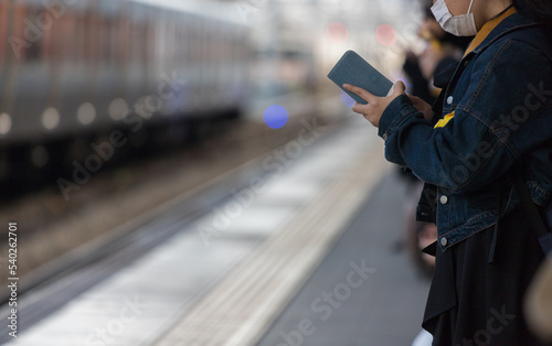 スマートフォンを弄る通勤電車を待っている人の姿