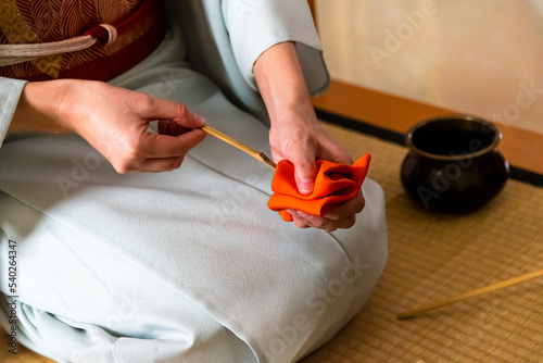 Japanese woman, tea master, Sen Rikyu, hands using an orange purifying cloth to clean a chashaku bamboo matcha tea spoon in Japanese traditional tea ceremony