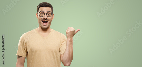 Banner of young man in t-shirt pointing with thumb to right side, feeling excited about great offer