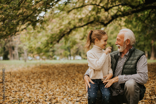 Grandfather spending time with his granddaughter in park on autumn day