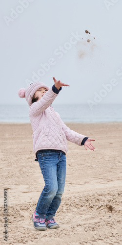 young girl is playing on an empty beach during a foggy, cold day