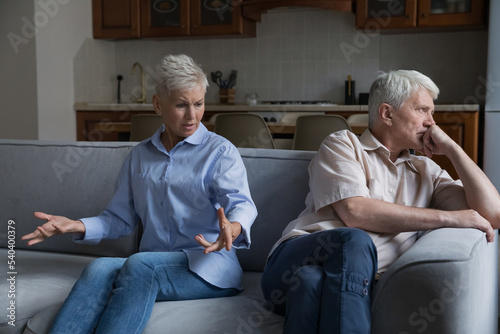 Wound up older wife expresses her displeasure to annoyed husband sit together on sofa at home. Aged wife and husband experiencing marital crisis, lack of understanding between mature spouses, quarrels
