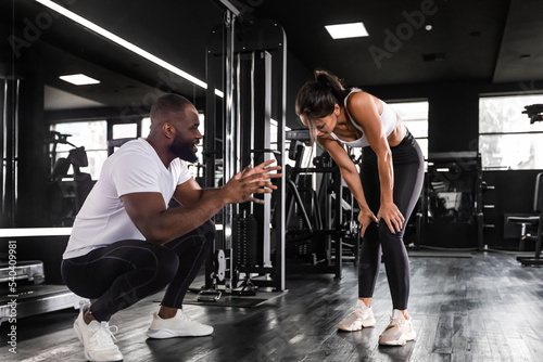 Fitness instructor exercising with his client at the gym, african man and caucasian woman.