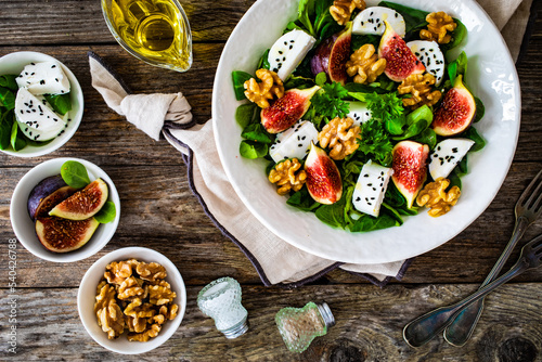 Fresh salad - goat cheese, fig, walnuts and leafy greens on wooden table 