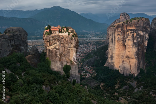 Brightly lit Christian monastery on cliff surrounded by mountain cliffs at sunset, Meteora, Greece