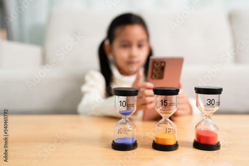 The sandclock with difference time in the background of little girl playing the smartphone. Concept of kid and technology and impact child development.