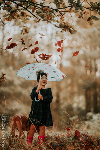 Dziewczynka w lesie trzyma parasol przed opadającymi liśćmi