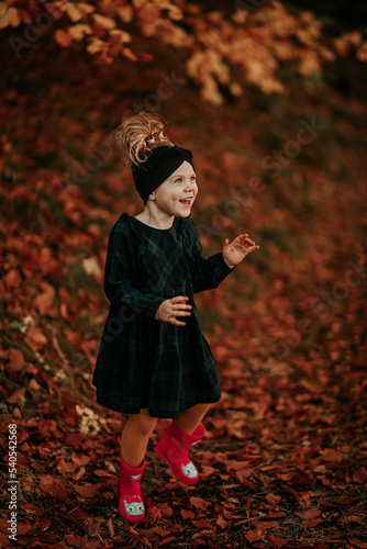 Mała dziewczynka bawi się w jesiennych liściach w lesie