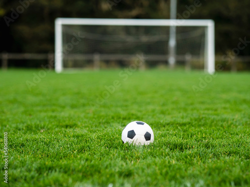 Classic soccer of football ball on the dark green grass field in focus. Goal post out of focus in the background. World wide popular sport activity.