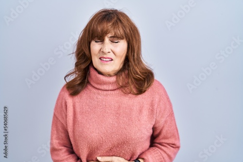 Middle age hispanic woman standing over isolated background with hand on stomach because indigestion, painful illness feeling unwell. ache concept.