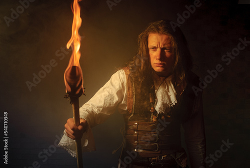 Young pirate filibuster with burning torch on dark brick background