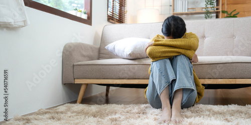 Hand on temples of young unhappy sadness Asian girl sitting on sofa. She is feeling not very good due to her sickness and having a headache. Seen from the front. Stress and sickness concept.