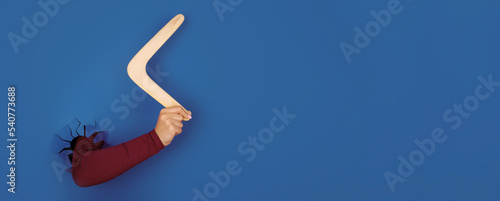 hand holding boomerang over blue background, panoramic layout
