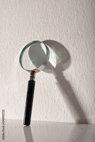 magnifying glass lean against white wall with shadow