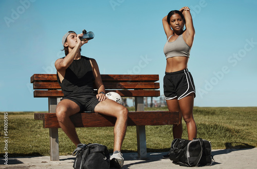 Man, woman and fitness break for stretching, drinking water or muscle recovery after training, exercise and workout. Soccer players, sports friends or football players in warmup in nature garden park