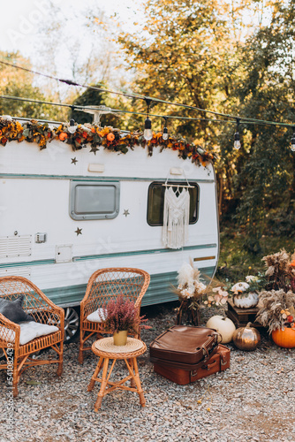 Wooden chairs and table placed outside cozy retro caravan on autumn day in countryside. Camping life concept