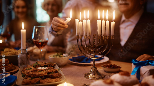 Close up of boy lights candles in menorah while celebrating Hanukkah with his family at dining table.