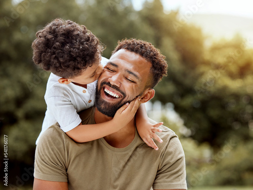 Father, bonding kiss and boy child hug happy in nature with quality time together outdoor. Happiness, laughing and family love of a dad and kid in a park enjoying nature hugging with care and a smile