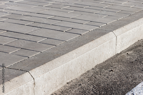 The sidewalk paved with concrete tiles is separated from the asphalt road by a concrete curb.