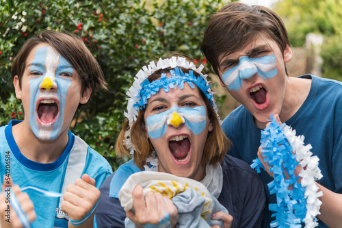 Familia con la cara pintada con los colores de la bandera Argentina, felices alentando al seleccionado en los partidos del mundial de futbol. 