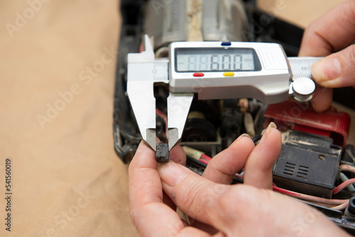 Manos con un calibrador digital, midiendo las escobillas de carbón de una herramienta eléctrica