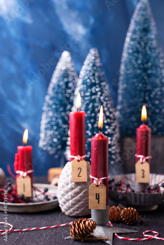 Lovely red and blue advent Christmas composition. Red burning candles, wild blue berries and blue decorative trees against blue textured background. Scandinavian minimalistic style. Still life