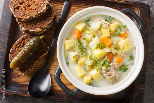 Zupa Ogorkowa Cucumber soup is a traditional Polish and Lithuanian soup made from sour, salted cucumbers and root vegetables closeup on the pot on the wooden tray. Horizontal top view from above