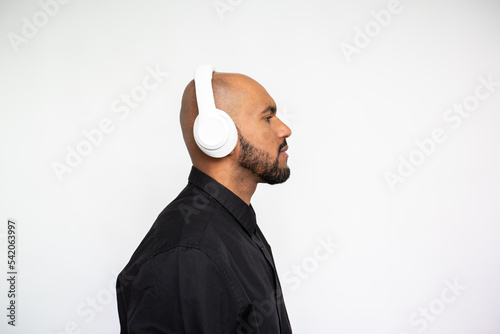 Side view of serious young man in headphones posing against white background. Bearded businessman wearing black shirt standing and looking away. Music and leisure concept