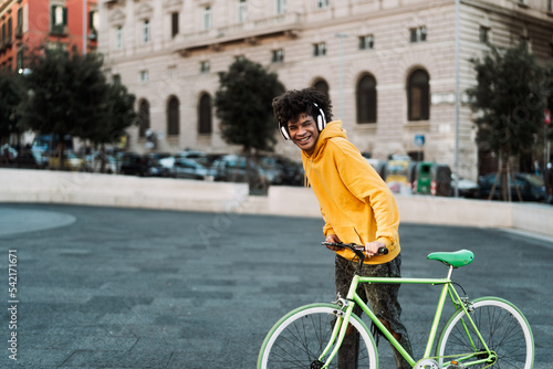 Happy young African man having fun with bike in the city while listening music with headphones - Youth millennial generation lifestyle and technology concept