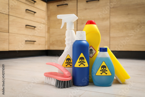 Bottles of toxic household chemicals with warning signs, scouring sponge and brush on floor indoors