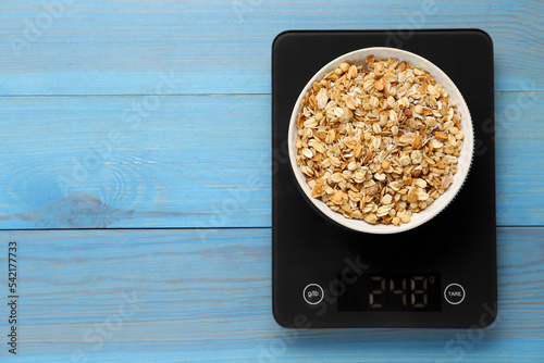 Digital kitchen scale with muesli on light blue wooden table, top view. Space for text